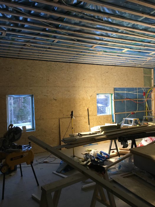 Inredning under konstruktion med OSB-paneler, synliga reglar i taket och arbetsmaterial på golvet.