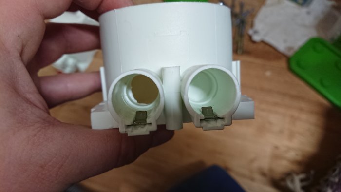 En hand håller en vit elektrisk dosa med två tomma utrymmen och spärrbleck designade för att hålla fast slangen.