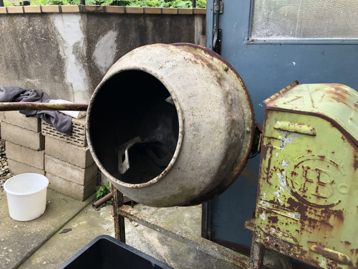 Gammal rostig betongblandare med öppen trumma utomhus, används vid renoveringsarbete.