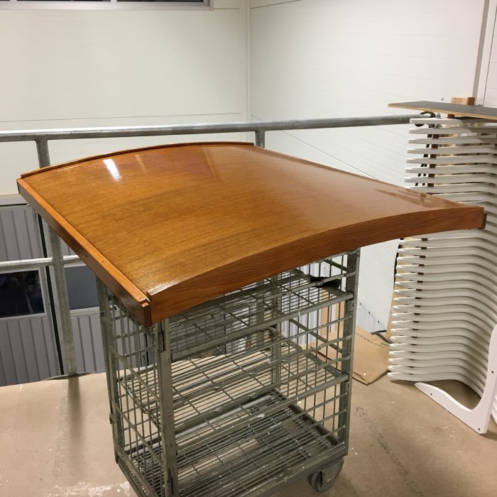 Träpanelad nedgångslucka till båt på en vagn, i ett verkstadsutrymme med vita väggar och delar i bakgrunden.