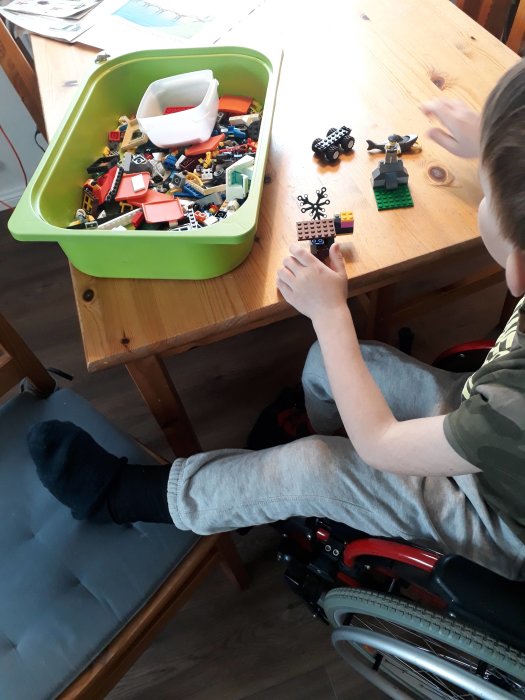 Barn i rullstol med gipsat ben leker med Lego på ett bord.