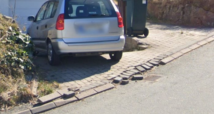 Skadad uppfart med lossade kantstenar och ojämnt liggande marksten framför en parkerad bil.