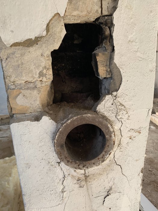 Söndervittrad vägg med ett gammalt inmurat rör som leder till en öppen spis eller kamin.