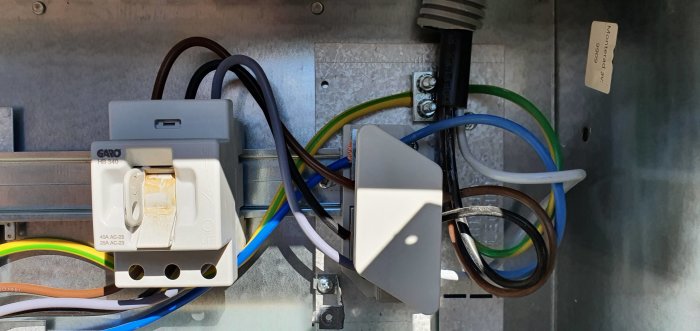 Inuti ett öppet fasadmätarskåp med fem ledare som ansluter till säkringar och kablar som kommer in från nedre vänstra hörnet.