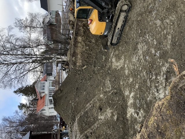 En stor grävmaskin nära en djup grop på en byggarbetsplats. Bilden är vinklad så grävmaskinen ser tippad ut.