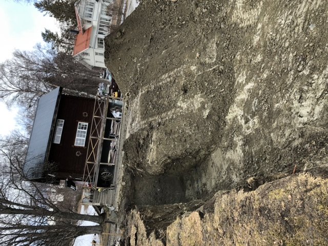 Stor grop i marken bredvid en byggnadsställning och hus, avsedd för byggprojekt, ca 3,1 meter på djupaste stället.