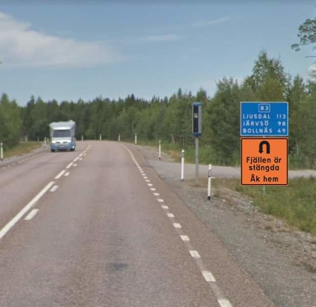 Svensk landsväg med vägskylt och handskriven skylt som säger "Fjällen är stängda Ak hem".