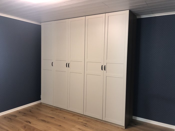 White wardrobes in a bedroom with blue walls and wooden flooring, recently fitted with minimal cutting required.
