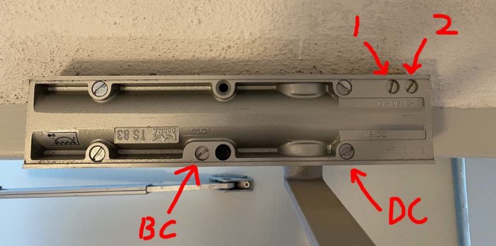 Öppen dörrstängare fäst vid en dörr med markerade justeringsskruvar och positioner BC och DC, utan synlig skada eller fel.