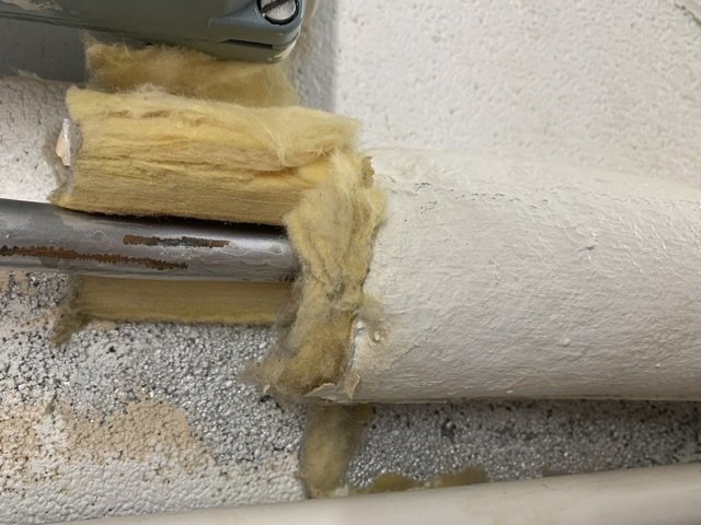 Skadad rörisolering av mineralull med gasbinda runt ett rör i ett pannrum, med synliga avskurna delar och målarfärg.