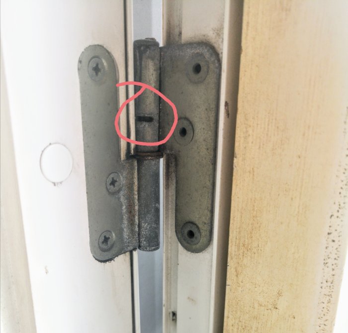 Dörrgångjärn med markerat smörjhål på en vit dörrkarm.
