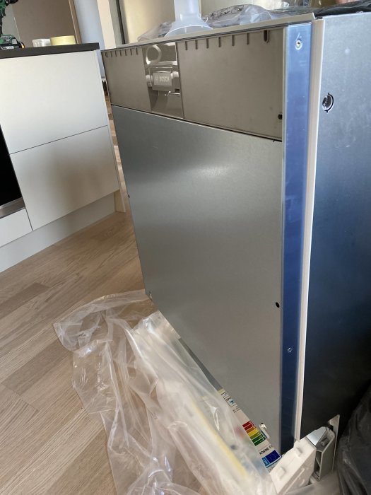 Bosch diskmaskin vilar på golvet med framsidan delvis täckt av en lucka och monteringsjärn synliga.