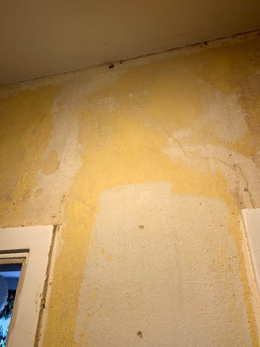 Nedsliten vägg med rester av gammalt tapetklister och synliga elkablar ovanför en dörrkarm.