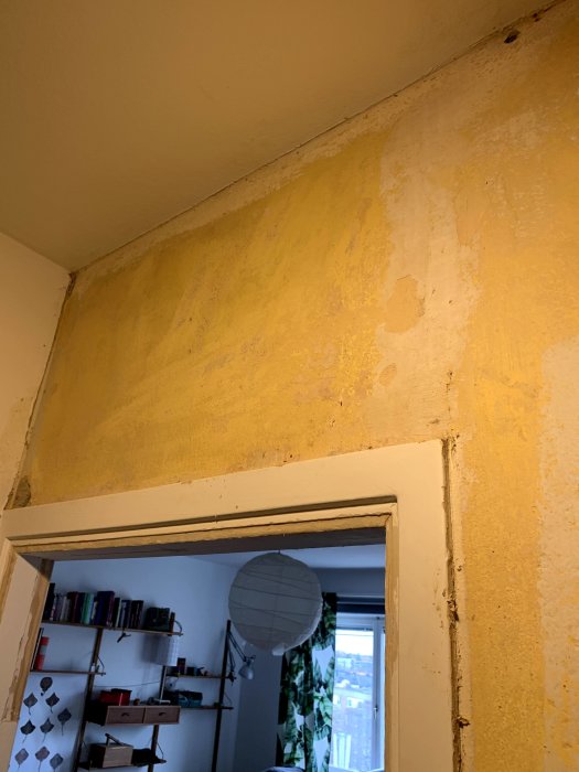 Vägg i hall under renovering med bortriven tapet, synliga elledningar och en spricka nära dörrkarmen.