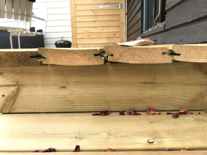 Synlig buckling av nyinstallerade träplankor för uteplats sett från en trappa med bladrester på golvet.