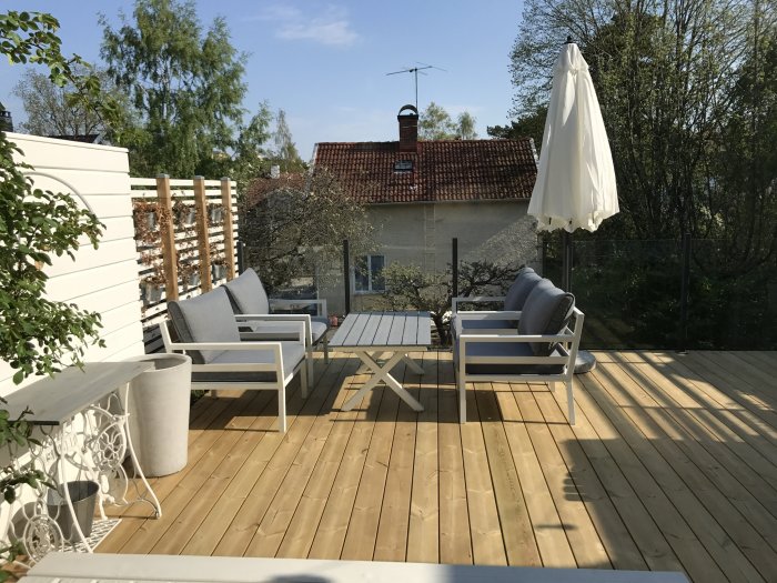 Nyinstallerad, skarvfri trätrall på en solig uteplats med utemöbler, paraply och en ej matchande planka synlig.