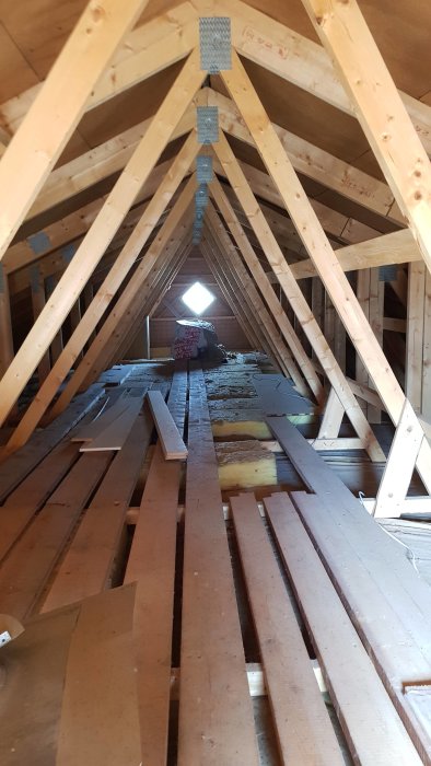 Kallvind med oisolerad takstolstruktur och snedsträvor, öppet takfönster och bråte på golvet.
