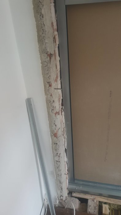 Ojämnt tegelvägg med ett metallprofil för dörrkarm och en gipsvägg under konstruktion.
