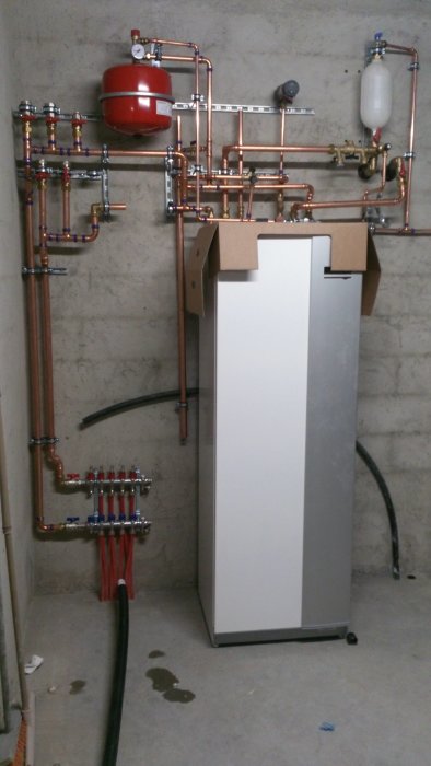 Installation av hemmavärmesystem med kopparledningar, expansionskärl, värmepump och slangar i källare.