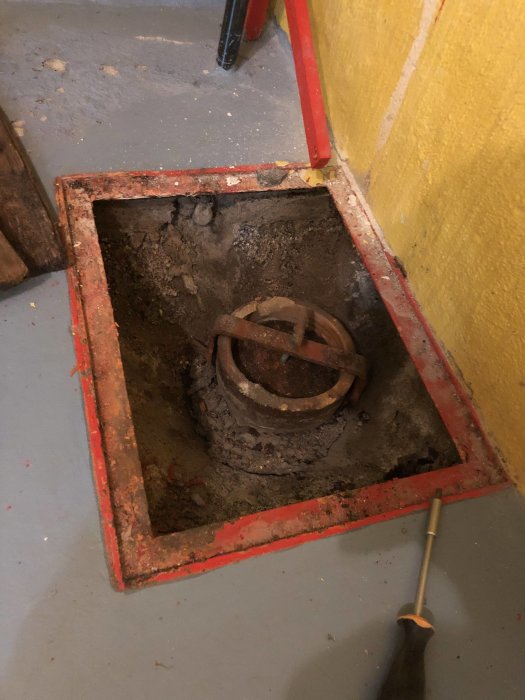 Öppen golvbrunn med gammalt rör av glaserat tegel eller betong i nedlagt pannrum under renovering.