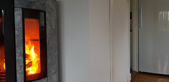 Kamin med brinnande eld och en synlig spricka på murstockens vita vägg när den är varm.