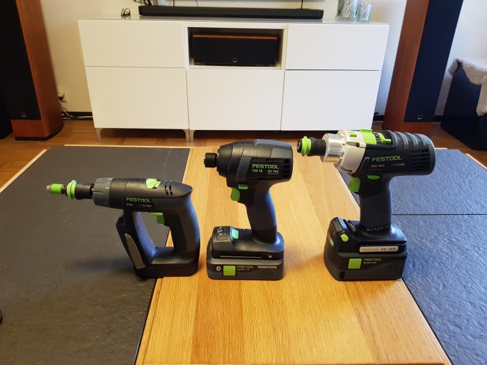 Tre batteridrivna Festool skruvdragare på ett bord framför en TV-bänk.