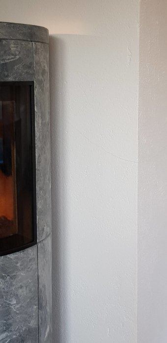 Vit vägg med en spricka bredvid en hörna av en mörk kamin.