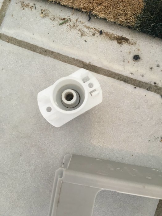 Ventil och plastdelar från torktumlare på ett smutsigt stengolv utomhus.