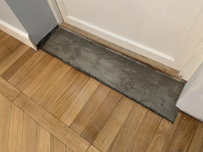 Renoveringsarbete med en utjämnad yta av vekt bruk vid en dörrtröskel mellan tegelvägg och trägolv.