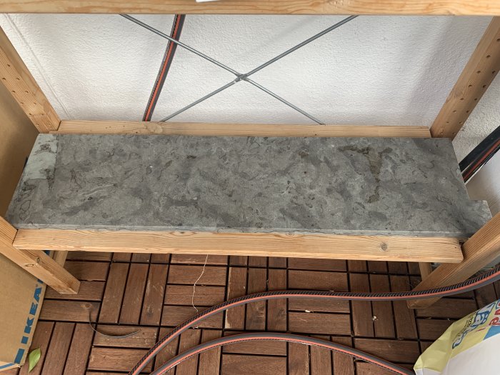 En kalkstenströskel vilande på en träställning inomhus, över en brun balkongplatta, med synliga kablar och verktyg.