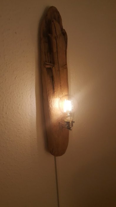 Träskulptur på vägg med glödlampa som lyser starkare än i verkligheten.