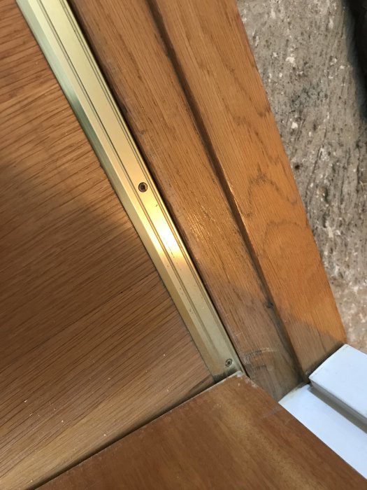 Närbild på parkettgolv som möts med en metalltröskel vid ett dörrparti.