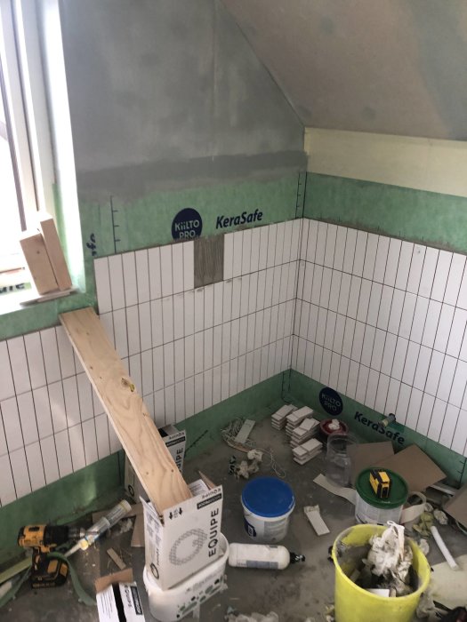 Badrum under renovering med halvsatt kakel, tätskiktsduk och byggmaterial på golvet.