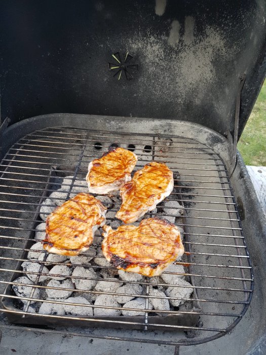 Fyra grillade kycklingfileer på en kolgrill markerar säsongens första grillning.