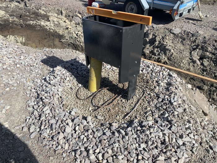 Monterat markmätarskåp på gjutet fundament med makadam runt och grävt område i bakgrunden.