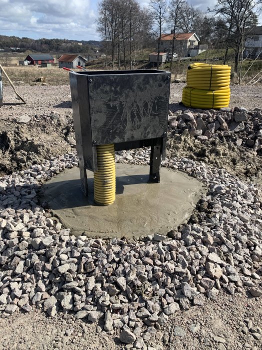 Markmätarskåp monterat på nygjutet fundament omgivet av makadam, med landskap i bakgrunden.