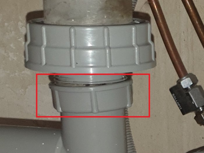 Grå inramad överfallsmutter på avloppsrör sitter snett, markerad med rött, vilket kan indikera en potentiell otäthet.