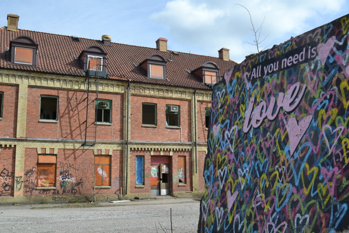 Nedgången byggnad med klotter, graffiti och texten "All you need is love" på en vägg i förgrunden.