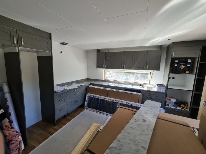Nytt uppgraderat kök under installation med gråa skåp, marmor bänkskivor och byggmaterial.