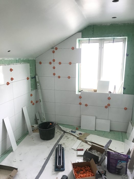 Pågående renovering av badrum med halvväggsbeklädnad av kakel, tätskikt och arbetsmaterial utspridda.