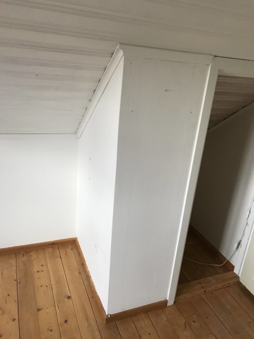 Vit stötta i hörn av ett rum med trägolv och snedtak, avsedd att stödja takstolarna.