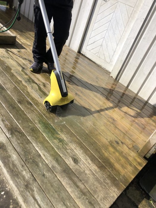 Man rengör en träaltan med högtryckstvätt, synlig skillnad på behandlad och obehandlad yta.