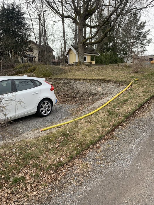 Nygrävd parkering med vit bil framför grön beklädd slänt och hus i bakgrunden.