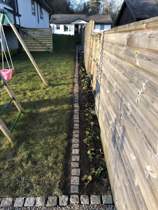 Nyinstallerad kantsten längs en trädgårdsgång bredvid ett trästaket.