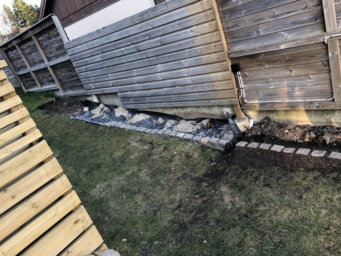 En nylagt kantsten längs med hus och altan, ojämna markarbeten synliga.