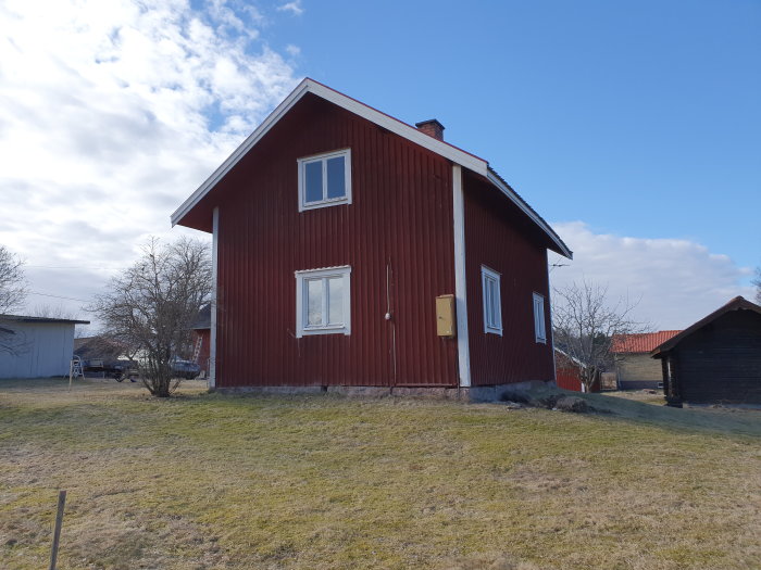 Rött timmerhus från 1870-tal med vita fönster och solig himmel, före renovering.