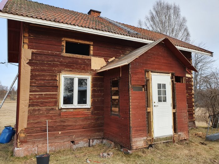 Renoveringsprojekt av en gammal timmerstuga med synliga rivningsarbeten på fasaden.