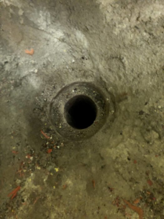 Rostigt lock i gjuten öppning med cirka 90mm innerdiameter och 140mm ytterdiameter.