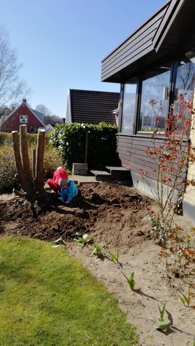 Två barn leker i en grävd jordhög bredvid ett uterum, förarbete för ett planerat altanbygge i en trädgård.