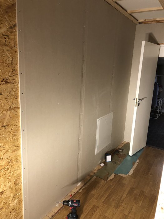 En vägg med gipsskivor framför OSB-panel med en liten öppning nedtill för rörinstallation.